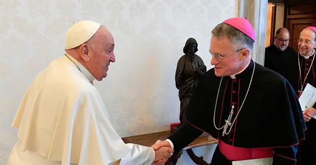 The image shows a formal greeting between a Pope and a bishop, with other clergy members in the background.