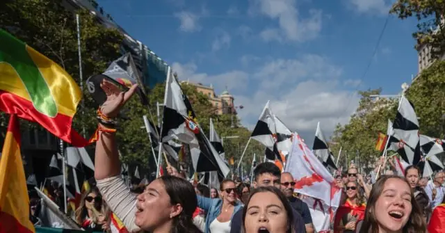 A vibrant crowd celebrates outdoors, waving flags and cheering under a clear blue sky.