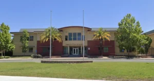 The image shows the exterior of Piner High School on a sunny day, with palm trees and a clear blue sky.
