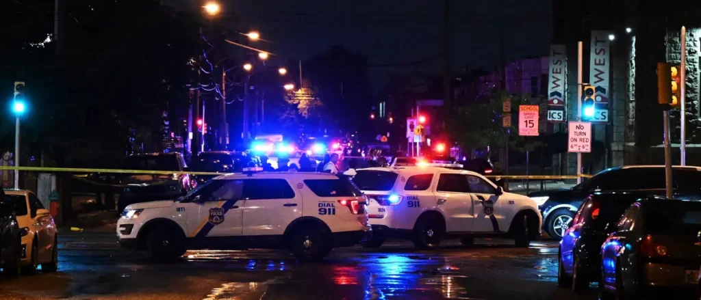A police investigation is underway at a nighttime scene with flashing lights and crime scene tape.