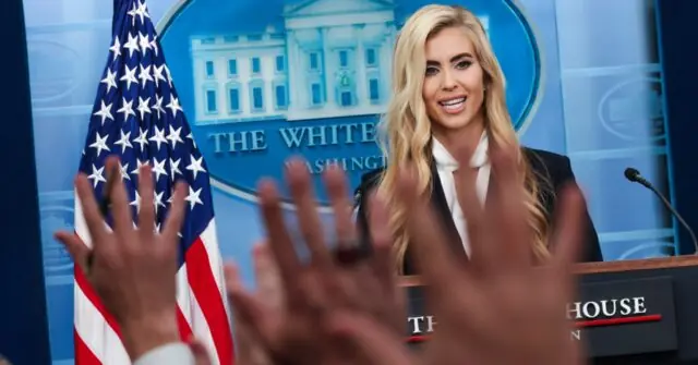 A person stands at a podium with the White House logo and an American flag in the background, with hands raised in the foreground.