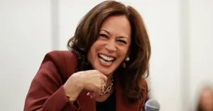 The image shows a person in a professional setting, smiling and gesturing with their hand, suggesting a moment of engagement or communication.