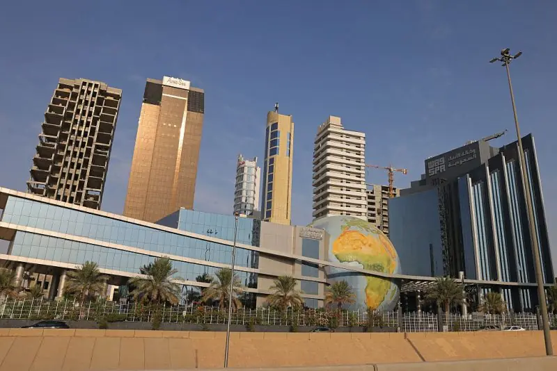The image shows a modern urban landscape with tall buildings, a large globe sculpture, and palm trees, under a clear blue sky.