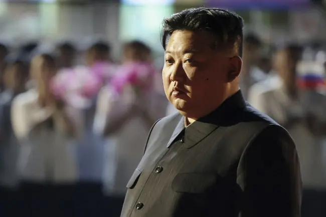 The image shows a man in a formal military-style uniform standing in front of a blurred crowd, suggesting a formal or official event.