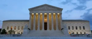 The image shows the United States Supreme Court building at dusk, illuminated by artificial lighting.