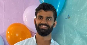 A man with a beard smiles in front of a colorful backdrop featuring balloons and a butterfly.