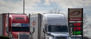 Two semi-trucks are parked at a Speedway gas station with fuel prices displayed on the sign.