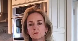 The image shows a person in a kitchen setting, with a microwave and oven visible in the background.