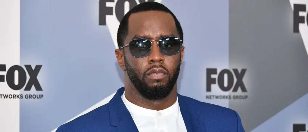 The image shows a person wearing a blue suit and sunglasses, standing in front of a backdrop with the Fox Networks Group logo.
