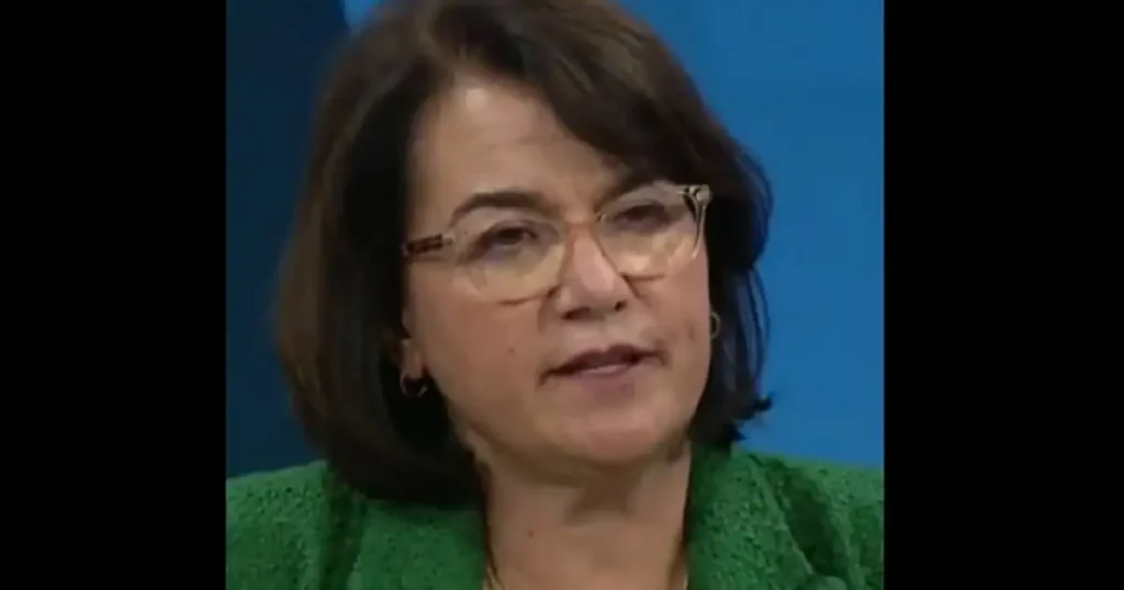 The image shows a person wearing glasses and a green top, set against a blue background.