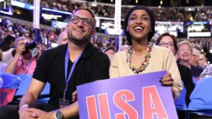 A man and a woman are seated in a crowd, smiling and holding a sign that reads "USA."