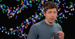 The image shows a person speaking in front of a colorful, abstract background.