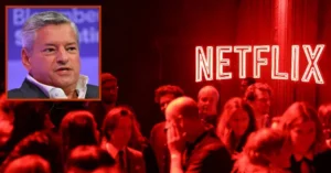 The image shows a man speaking at a Bloomberg event, with a crowd of people in the foreground and a Netflix logo illuminated in the background.
