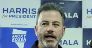 The image shows a man speaking in front of campaign signs for "Harris for President" and "Jacky Rosen U.S. Senate."