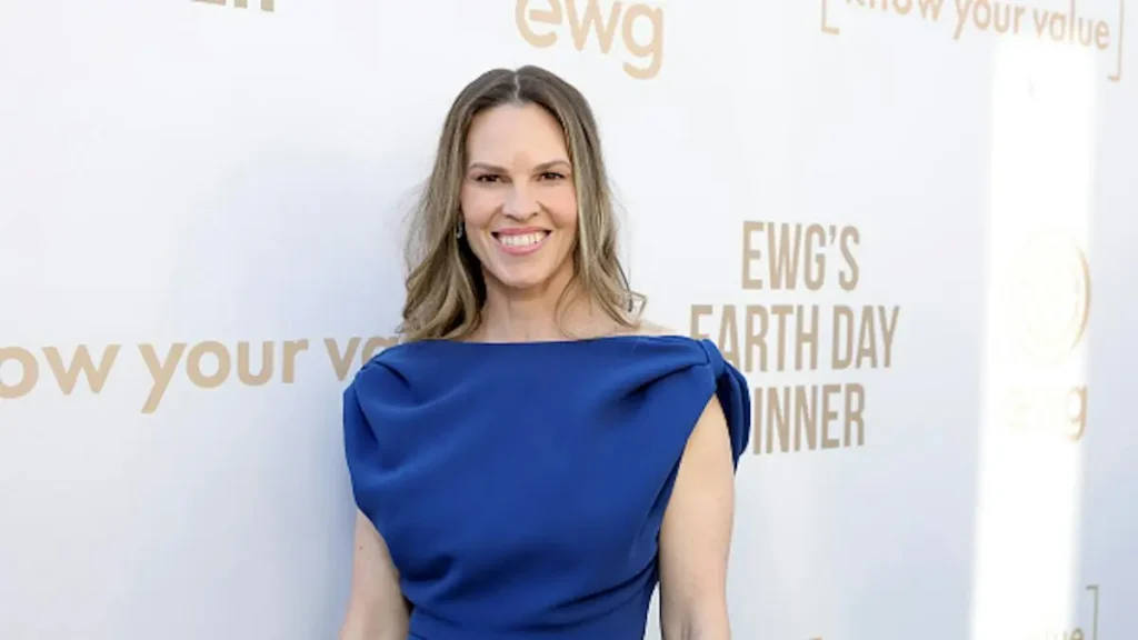 The image shows a person in a blue dress at an event with a backdrop that includes the text "EWG's Earth Day Dinner."