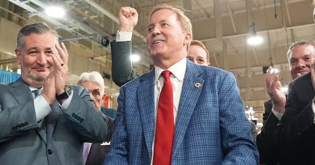 A man in a blue plaid suit raises his fist in a gesture of triumph or solidarity, surrounded by others who are clapping and smiling.