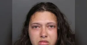 The image appears to be a mugshot of a person with long, dark hair.