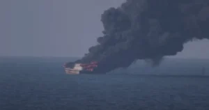 A ship is engulfed in flames and emitting thick black smoke into the air.