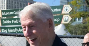 An older man smiles in front of directional signs pointing to various locations, including "Museum Campus," "Soldier Field," and "Dog Friendly Area."
