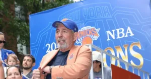 A man wearing a New York Knicks cap and jacket is seen in front of a banner celebrating the New York Knicks NBA championship.