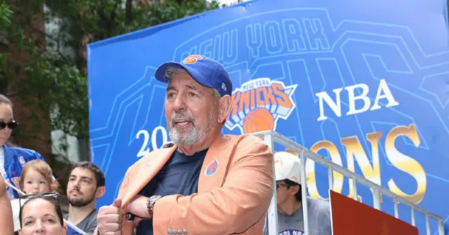 A man wearing a New York Knicks cap and jacket is seen in front of a banner celebrating the New York Knicks NBA championship.