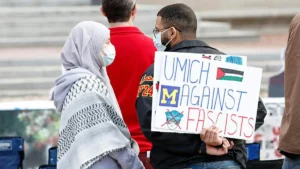A protestor holds a sign reading "UMICH AGAINST FASCISTS" during a demonstration.