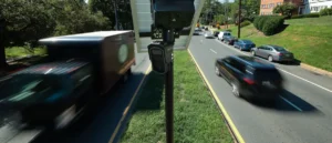 A speed camera is positioned on the side of a road, capturing vehicles as they pass by.