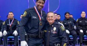 The photo captures a moment of celebration at a police graduation ceremony, with two officers in uniform smiling and posing for the camera.