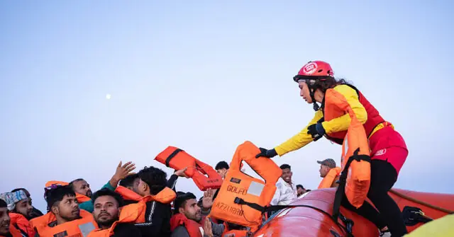 A rescue worker assists migrants on a life raft during a rescue operation at sea.