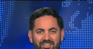 The image shows a person with a beard and short hair, set against a blue background with a dotted pattern.