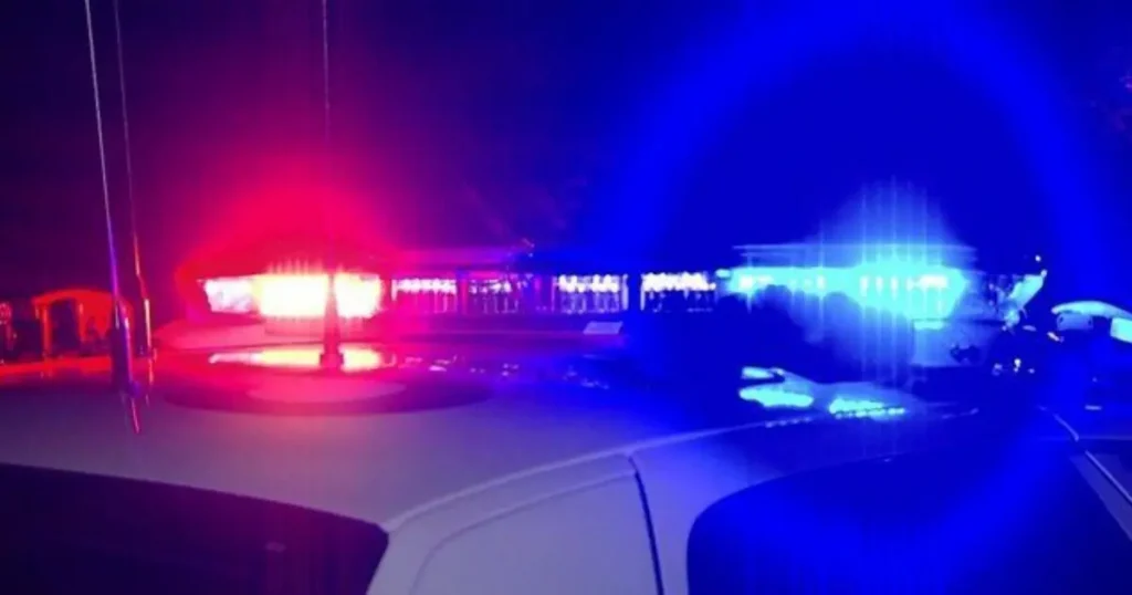 A police car with flashing red and blue lights is shown at night, indicating an emergency response.
