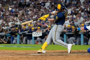 A baseball player swings at a pitch during a game, with a crowd of spectators in the background.