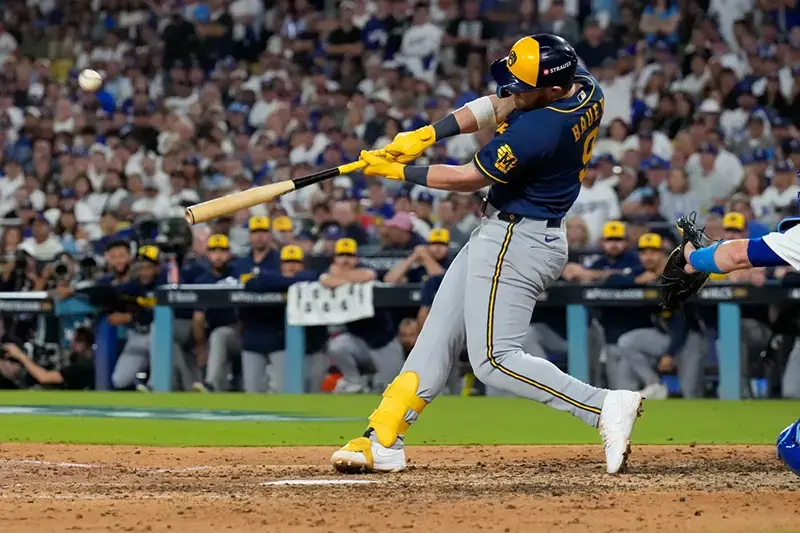 A baseball player swings at a pitch during a game, with a crowd of spectators in the background.