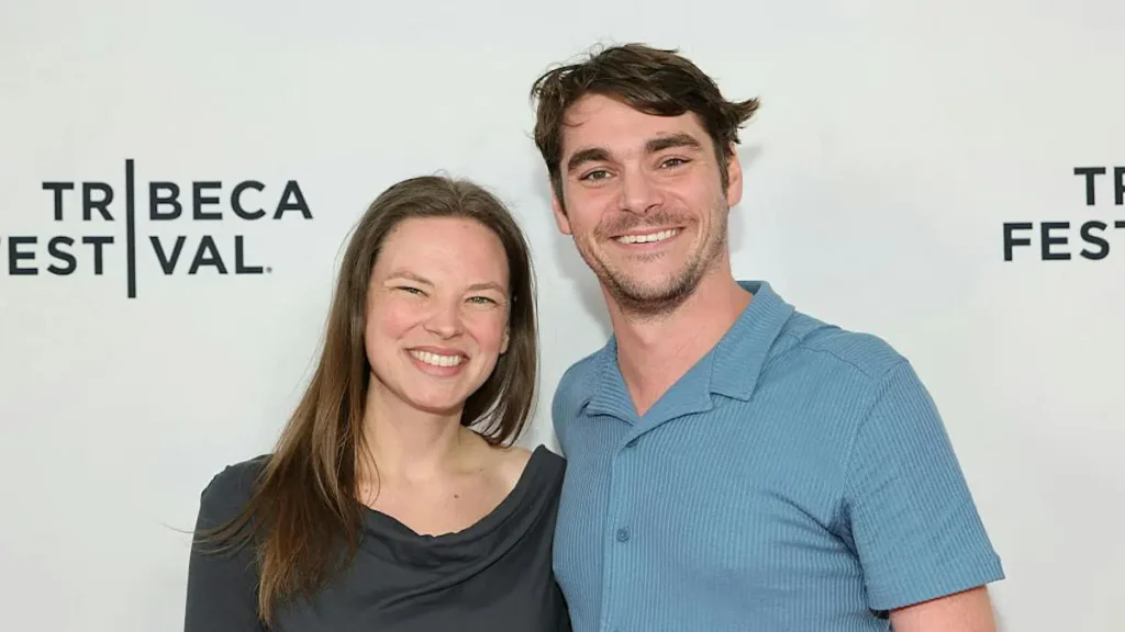The photo shows two individuals smiling at the camera in front of a backdrop for the Tribeca Festival.