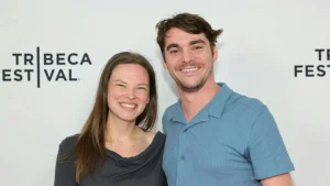 The photo shows two individuals smiling at the camera in front of a backdrop for the Tribeca Festival.