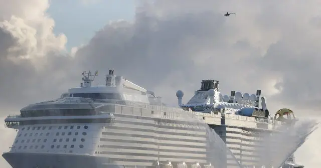 A large cruise ship is being sprayed with water, likely as part of a naming ceremony or celebration.
