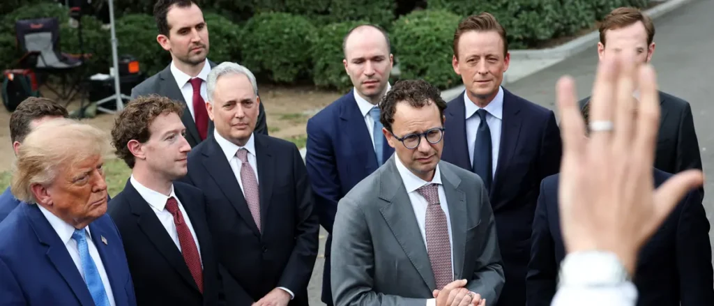 A group of men in suits and ties are gathered outdoors, with one person raising their hand in the foreground.