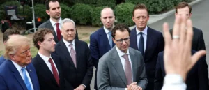 A group of men in suits and ties are gathered outdoors, with one person raising their hand in the foreground.