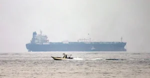 A small motorboat speeds across the water in the foreground, with a large tanker ship visible in the background.