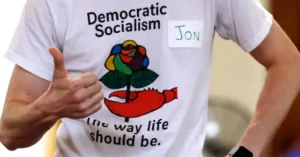 The photo shows a person wearing a shirt that promotes democratic socialism, with the text "The way life should be" and a graphic of a rose and a hammer and sickle.