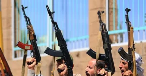 A group of individuals raise their AK-47 rifles in a public display, possibly during a demonstration or parade.