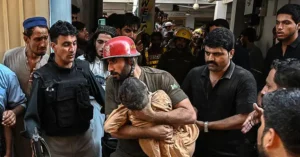 A rescue worker carries an injured person amidst a crowd of onlookers and emergency personnel.