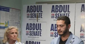 The photo shows a political event with campaign signs for "Abdul for US Senate" in the background.