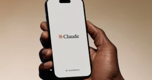 A hand holds a smartphone displaying the "Claude" logo by Anthropic.