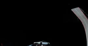A futuristic white car is suspended in mid-air, seemingly defying gravity, with a dark background and a curved structure on the right.