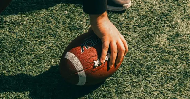 A close-up of a hand gripping an American football on a grassy field.