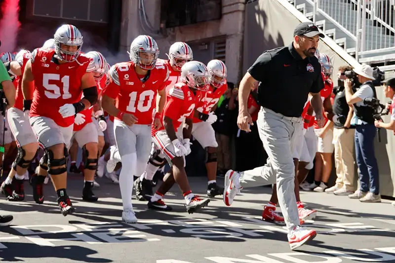 A football team, led by their coach, runs onto the field for a game.