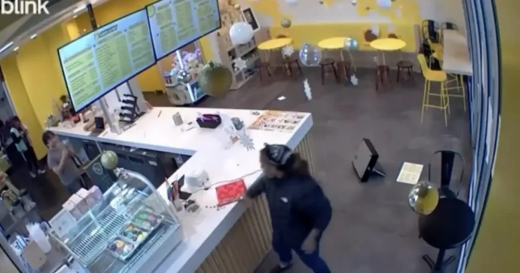 The image shows a brightly lit ice cream shop with a counter, menu boards, and a customer interacting with the staff.