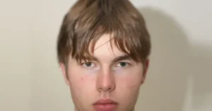 The image shows a close-up of a person with light brown hair and blue eyes, set against a plain background.