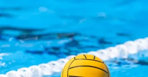 A yellow water polo ball is floating in a pool with lane dividers in the background.